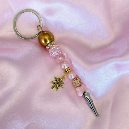 Pink and gold beaded roach clip with rhinestones and a gold cannabis leaf charm, handmade by Trap Mami LA.