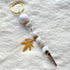 White and gold beaded roach clip with rhinestones and a gold cannabis leaf charm, handmade by Trap Mami LA.