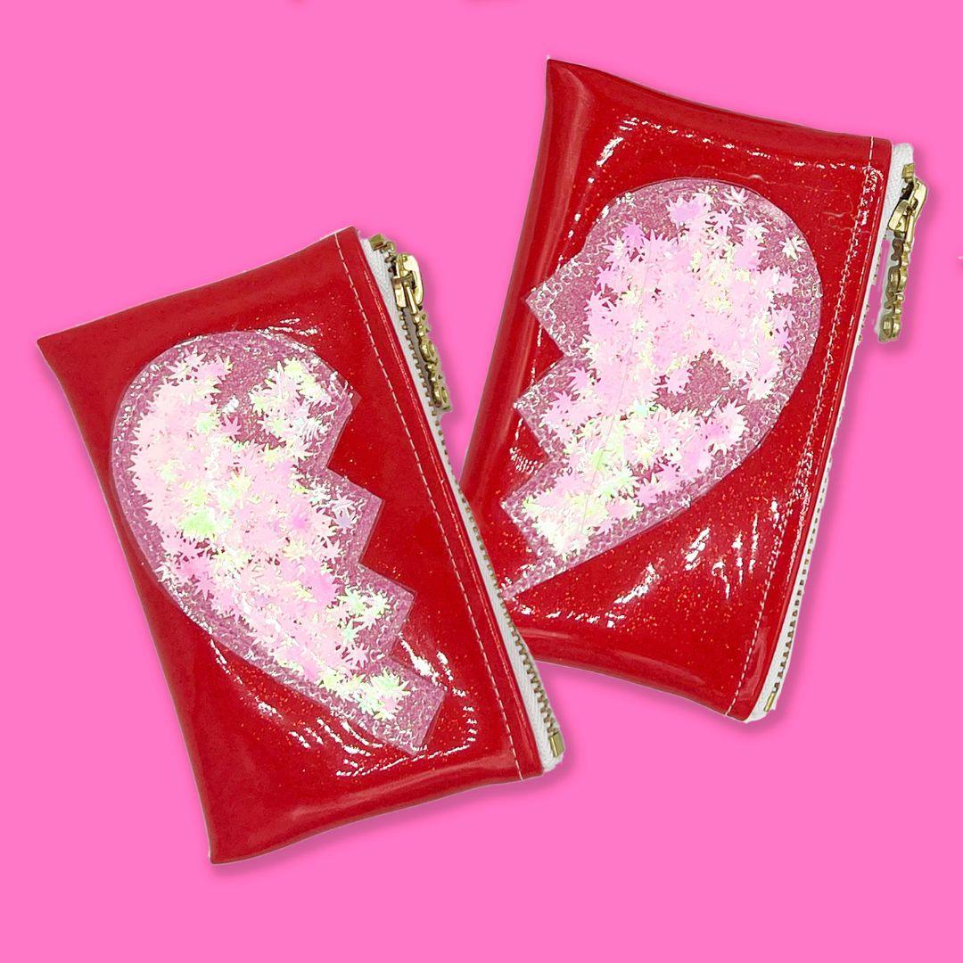 Two part glitter infused Best Buds Kush Klutch set in red with pink glitter broken heart design and cannabis leaf confetti, clear vinyl overlay and gold zippers, designed by Julie Mollo