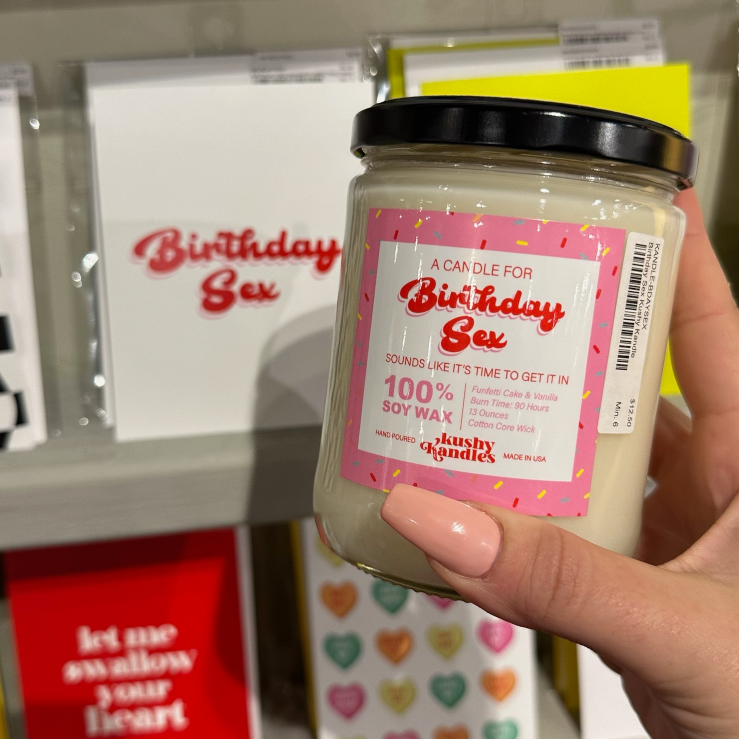 A hand holding the &quot;Birthday Sex&quot; soy wax candle with funfetti cake and vanilla scent, displayed against a backdrop of birthday-themed cards and gifts.