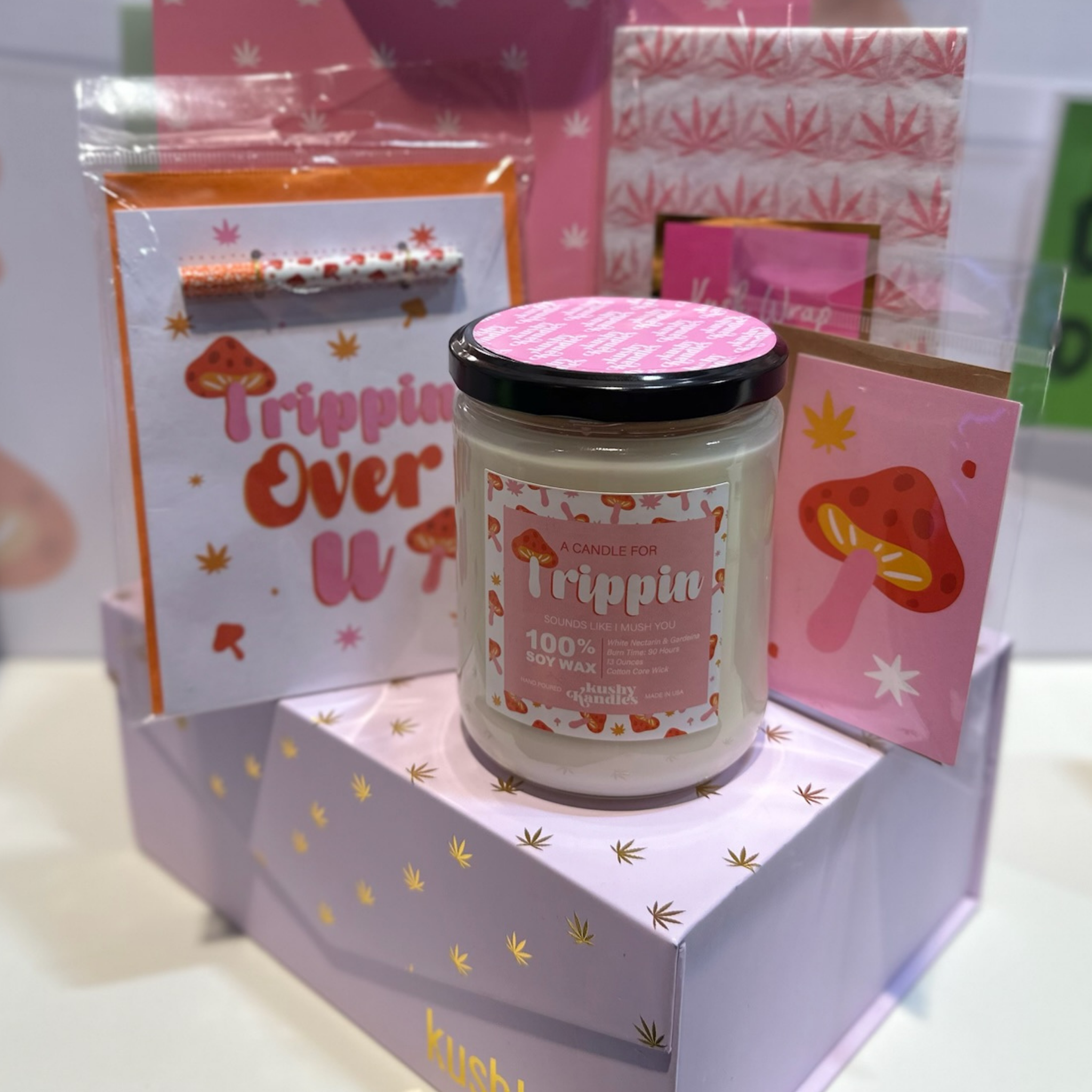 A &quot;Trippin&quot; soy wax candle with white nectarine and gardenia scent displayed among pink and mushroom-themed gifts, evoking a fun and whimsical atmosphere.