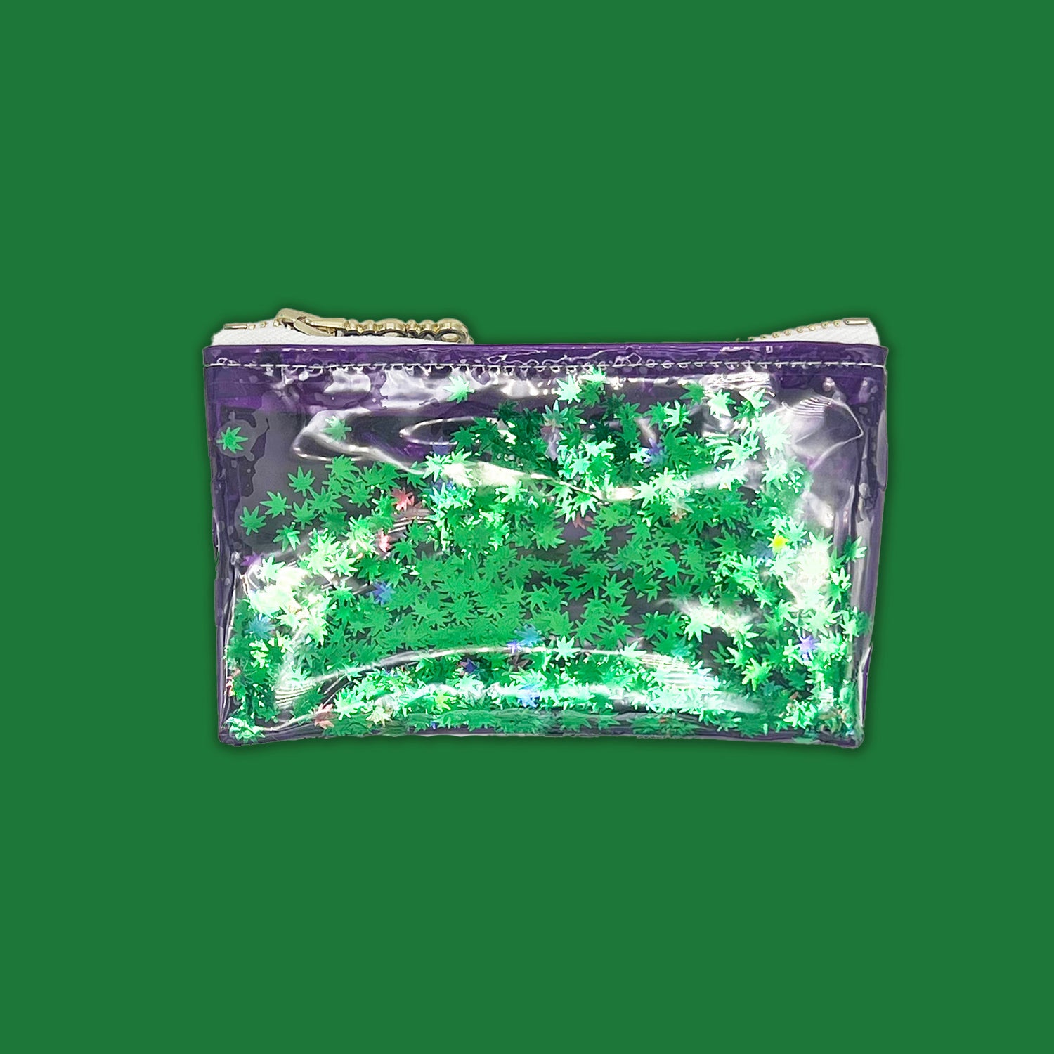 A stylish clear vinyl keychain clutch filled with floating green cannabis leaf confetti. Featuring a deep purple trim and a silver zipper, this compact and fun accessory is designed by Julie Mollo in collaboration with KushKards, perfect for stashing small essentials with a playful touch.