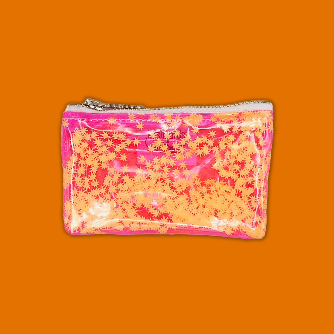 A vibrant, clear vinyl keychain clutch filled with floating orange cannabis leaf confetti. Designed by Julie Mollo in collaboration with KushKards, this playful mini bag features a pink trim and a silver zipper, making it a stylish stash for essentia